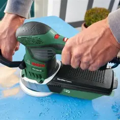 Ręce trzymają zieloną szlifierkę Bosch PEX 400 AE, która jest idealna do prac z drewnem.