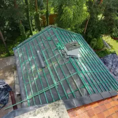 Remont dachu w trakcie. Czy przedłużenie dachu wymaga pozwolenia? Na zdjęciu widać konstrukcję dachu, materiały budowlane i otaczającą zieleń.