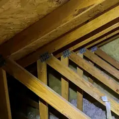 Drewniana konstrukcja dachu z widoczną izolacją. Widać krokwie i przestrzeń między murłatą a dachem, gdzie znajduje się wełna mineralna.