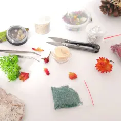 Materiały do tworzenia ozdób z żywicy epoksydowej: mech, suszone kwiaty, brokat, folia, pęseta, nożyczki.