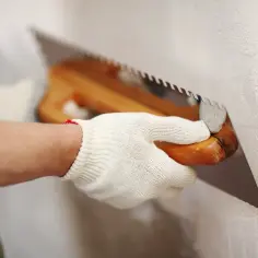 Ręka w rękawicy nakłada cienkowarstwową żywicę epoksydową do ścian za pomocą kielni.