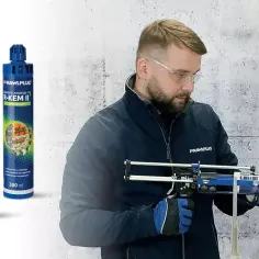 Mężczyzna w okularach ochronnych używa pistoletu do kotwy chemicznej, aplikując ją do otworu w betonie.