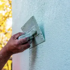 Pracownik nakłada tynk na elewację ze styropianu. W tle jesienne liście.