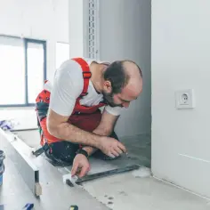 Majster precyzyjnie układa płytki przy drzwiach wejściowych, używając poziomicy i lasera.