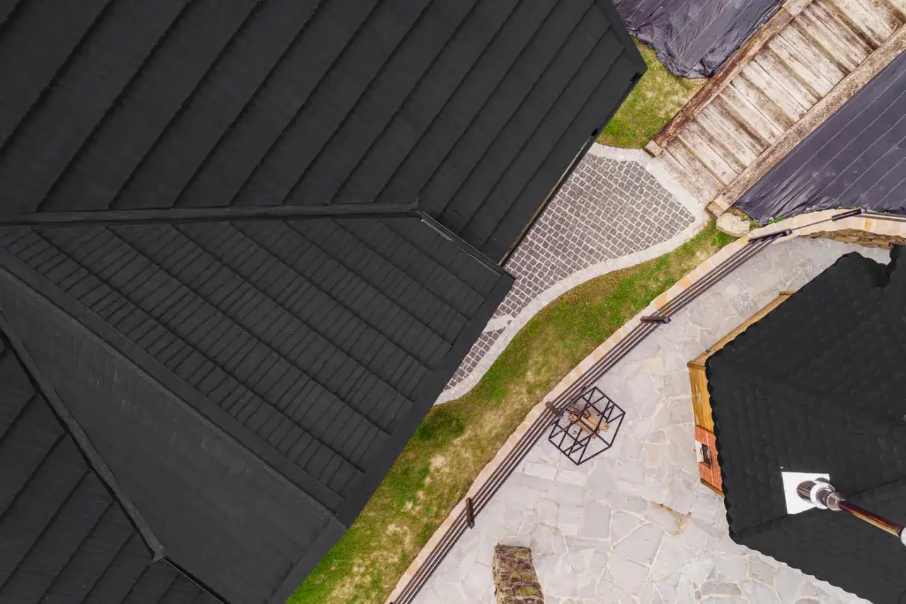 Czarne, łupkowe kamienie na dachu domu tworzą nowoczesny wygląd. Obok ścieżka z kostki brukowej i kamienne patio.