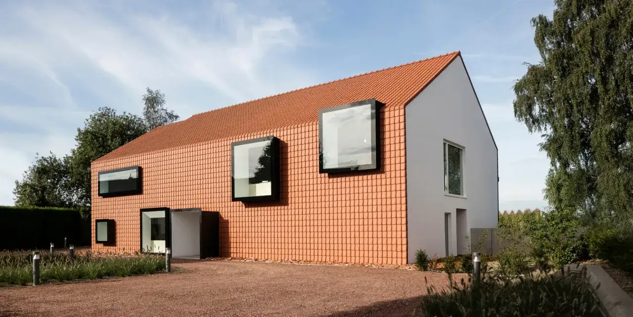 Nowoczesny dom z pomarańczowym, ceramicznym dachem i nietypowymi oknami.