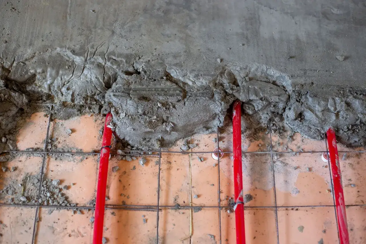 Budowa podłogi z ogrzewaniem: czerwone rurki grzewcze pod mokrym cementem, gotowe na wylewki. Jaki cement na wylewki będzie najlepszy?