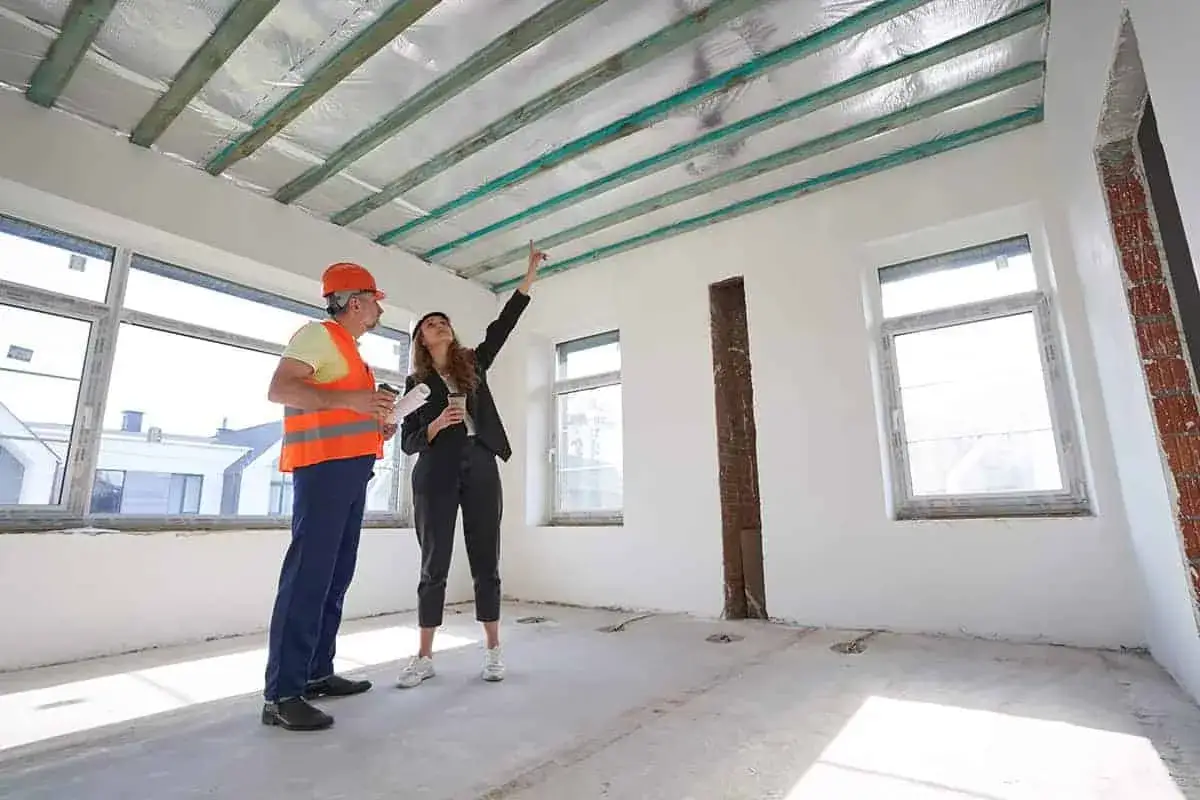 Inżynier i architektka omawiają montaż sufitu z karton gipsu. Widać drewnianą konstrukcję stropu z izolacją.
