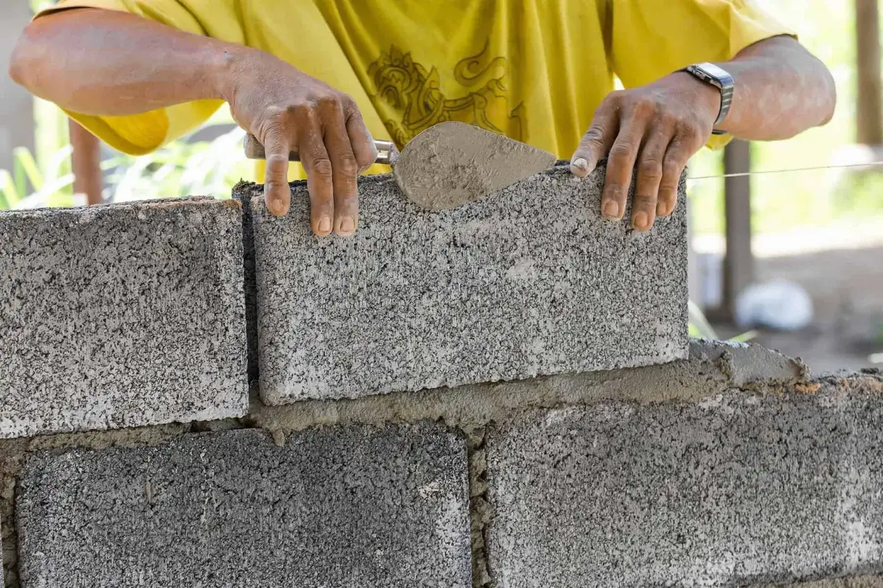 Murarz układa bloczki betonowe, tworząc solidną ścianę.
