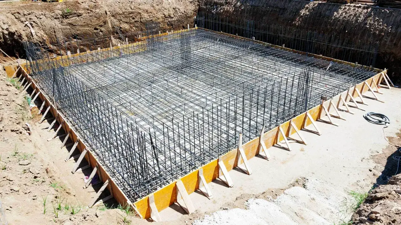 Siatka zbrojeniowa na ławie fundamentowej, gotowa do zalania betonem. Widać szalunek i pionowe pręty. To kluczowy etap, jak krecic zbrojenie.