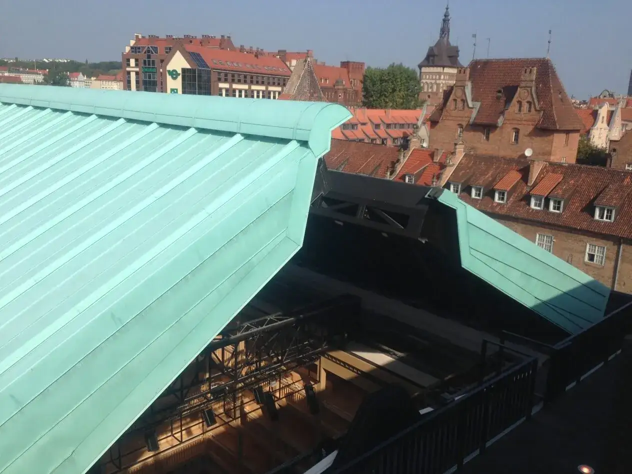 Zielony dach z miedzi nad nowoczesną konstrukcją, w tle zabytkowa zabudowa miejska.